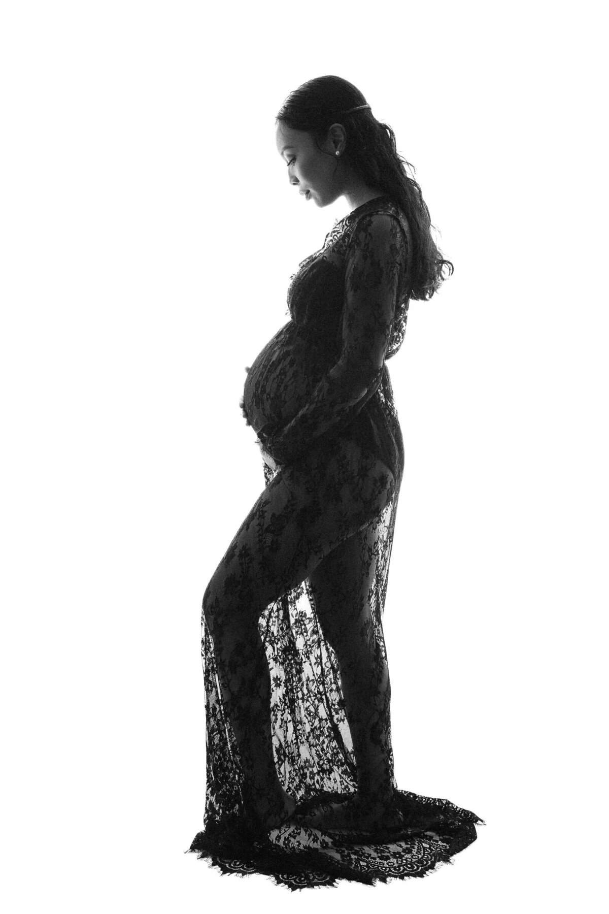 A woman in a long lace dress holding her pregnant stomach.