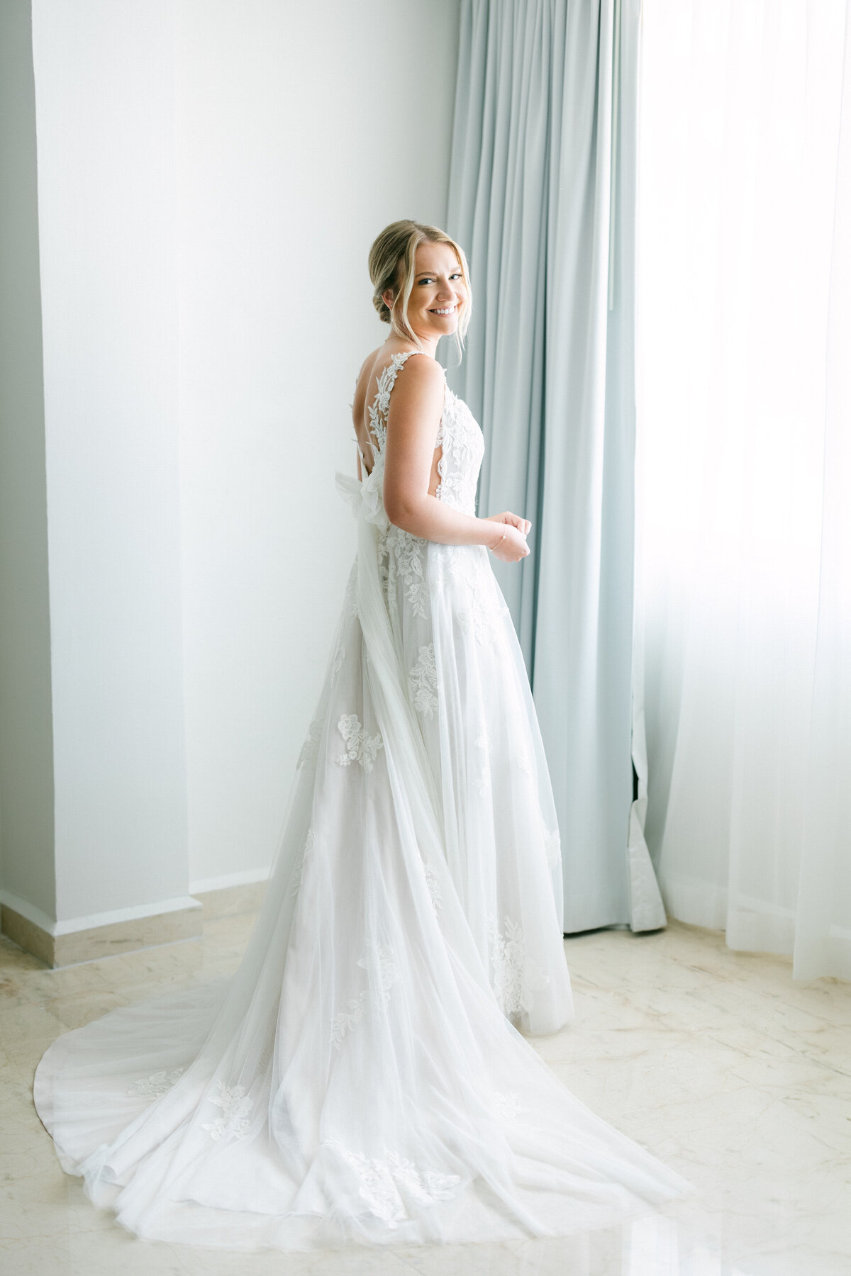 Bride smiling softly by the window in her lace gown before her Cancun wedding, photographed by Philadelphia photographer.