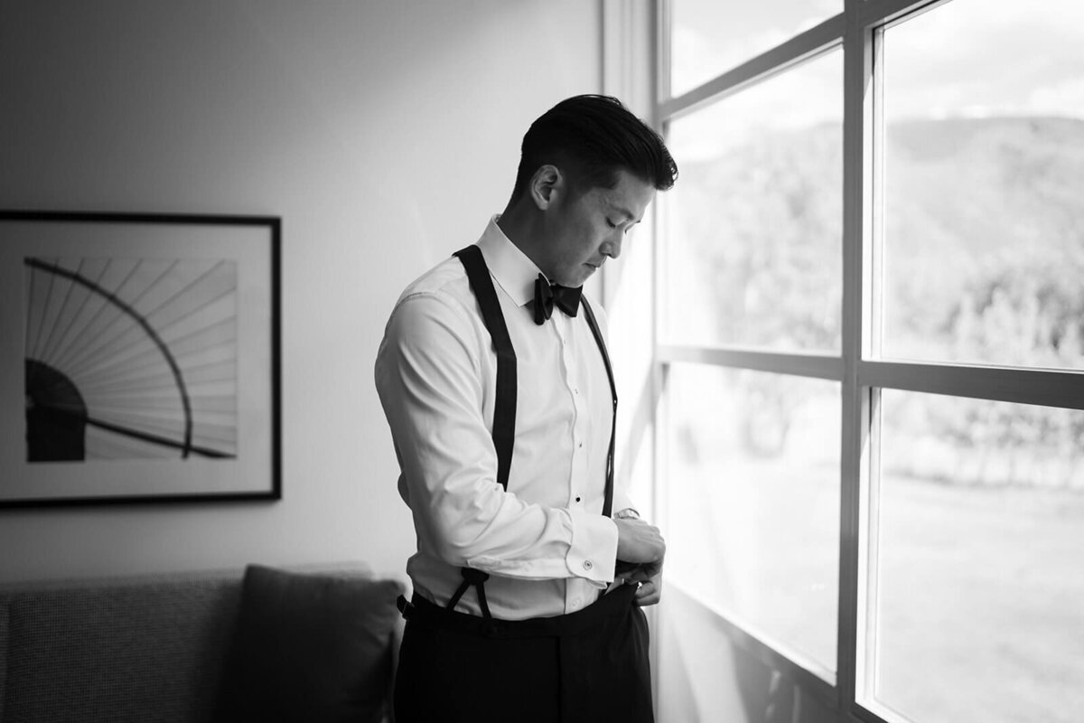 Groom getting ready at Aspen Meadows Resort, adjusting his suspenders in a light-filled room with a calm and elegant atmosphere.