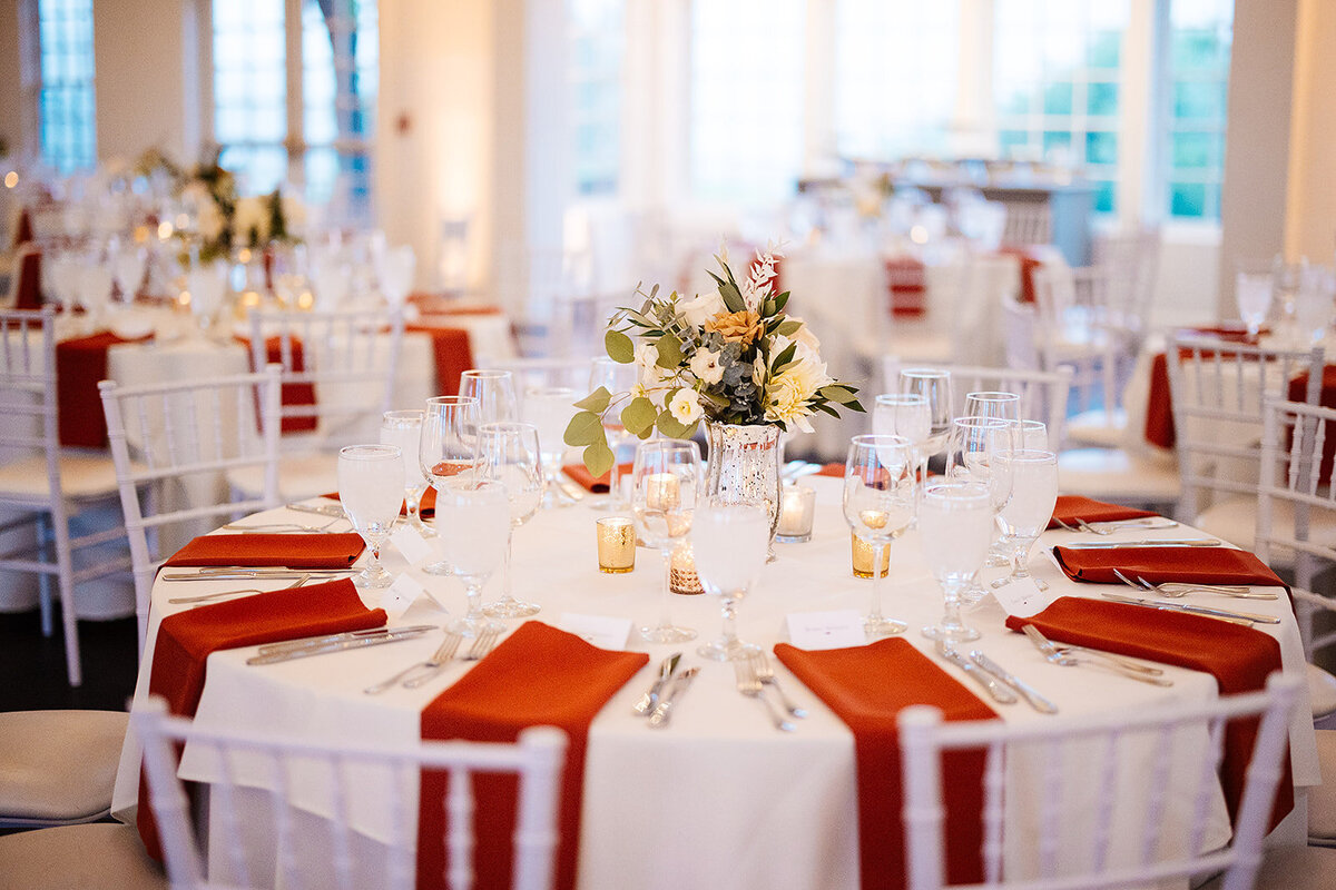 Red napkins with white and orange centerpieces at a wedding reception.