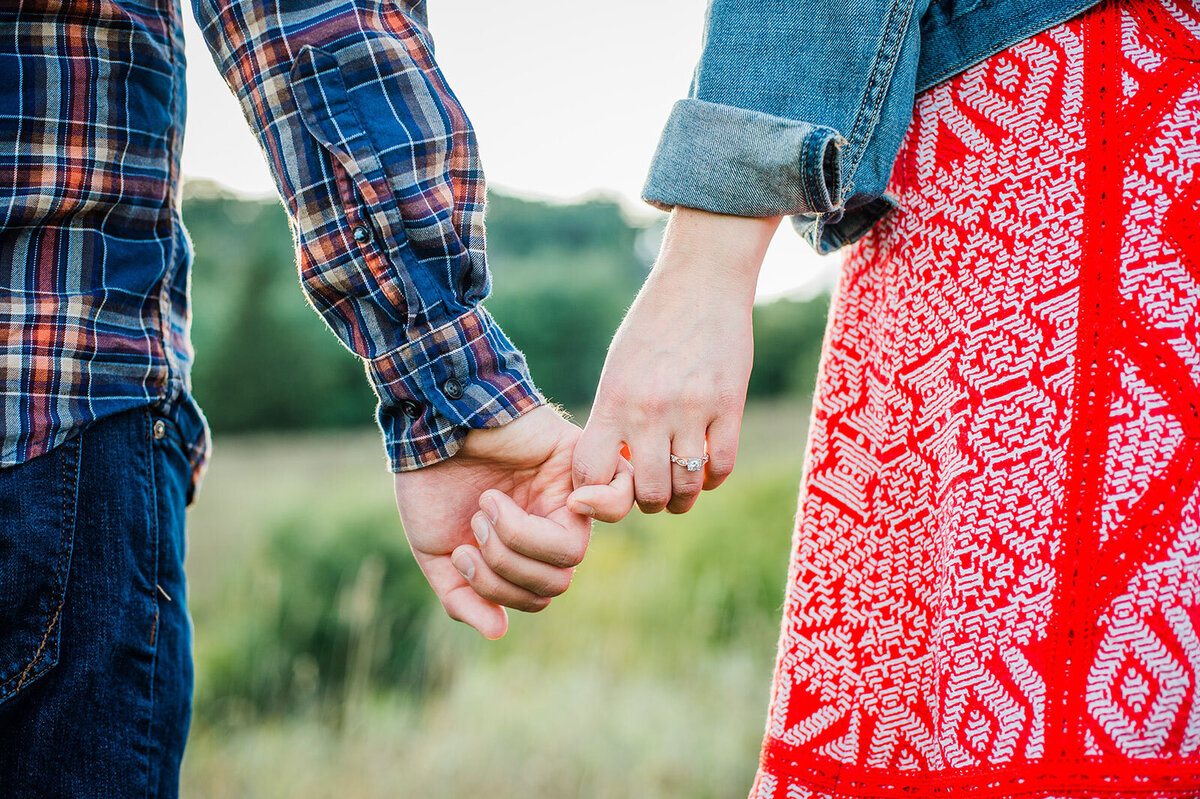 engaged couple holding hands in field with diamond ring