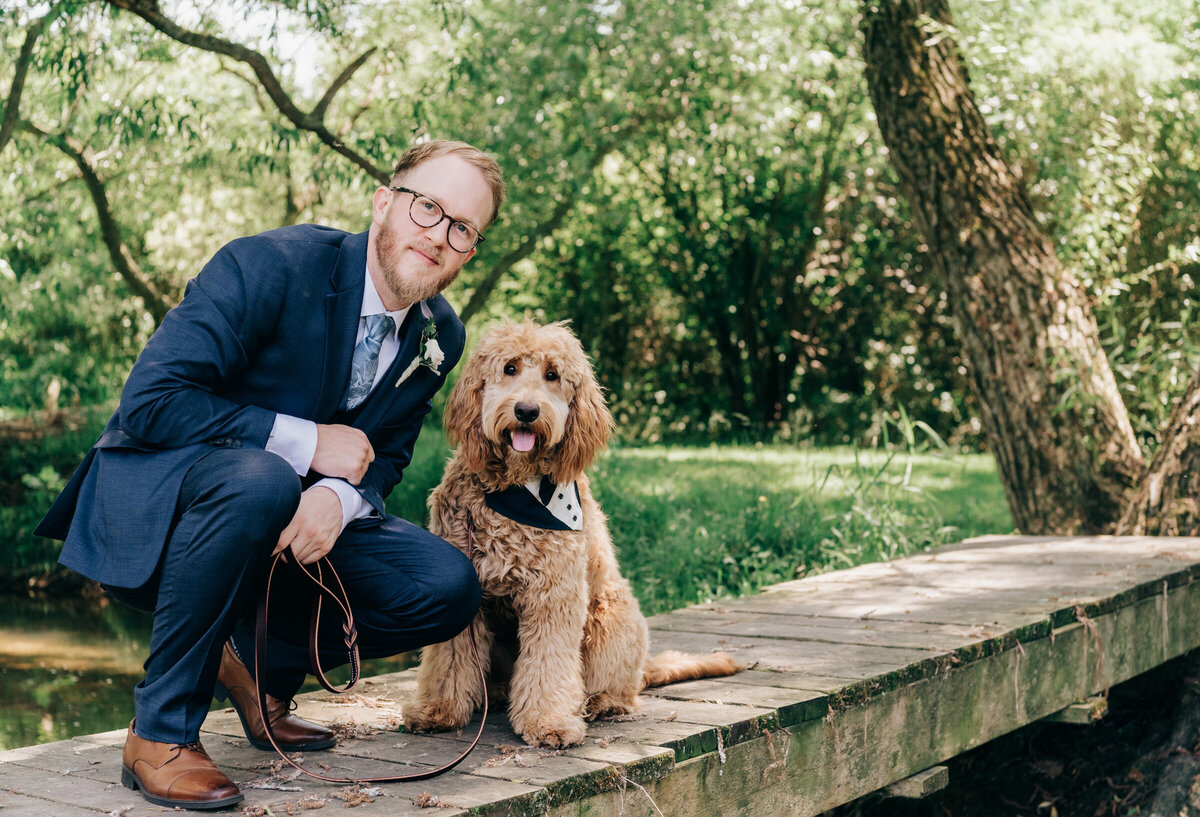 Groom poses with dog in tuxedo for outdoor wedding portraits
