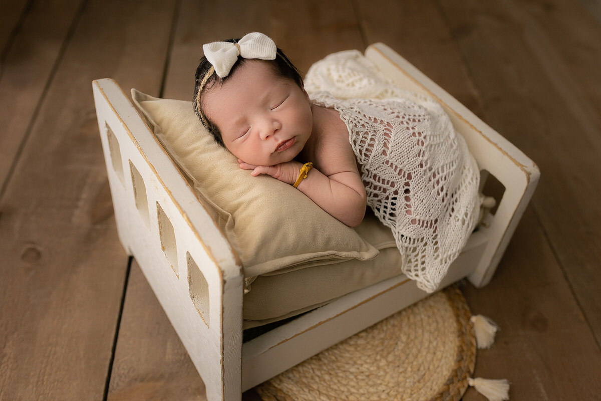 baby girl in tiny wooden bed gets newborn photos taken in Hamilton, ON