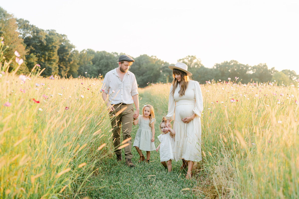 Family in neutral clothing walks in a field of tall wildflowers at sunset outside of Philadelphia