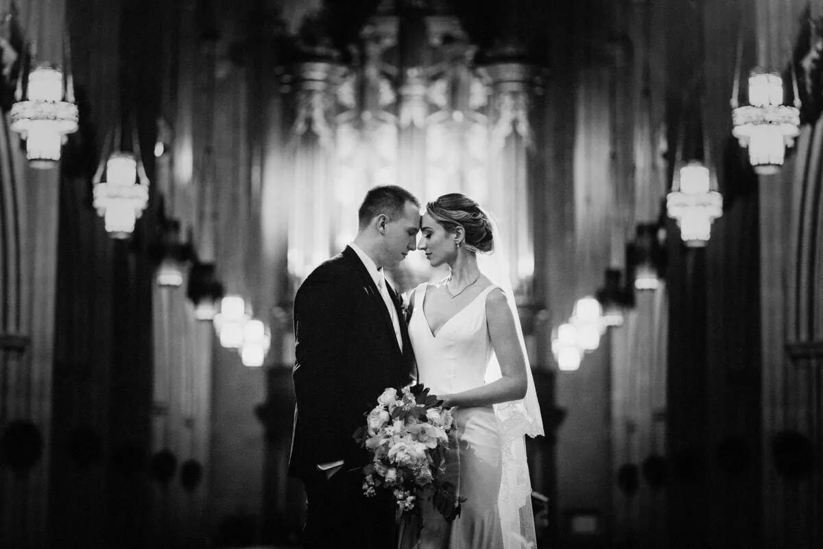A bride and groom standing forehead to forehead in a chapel.