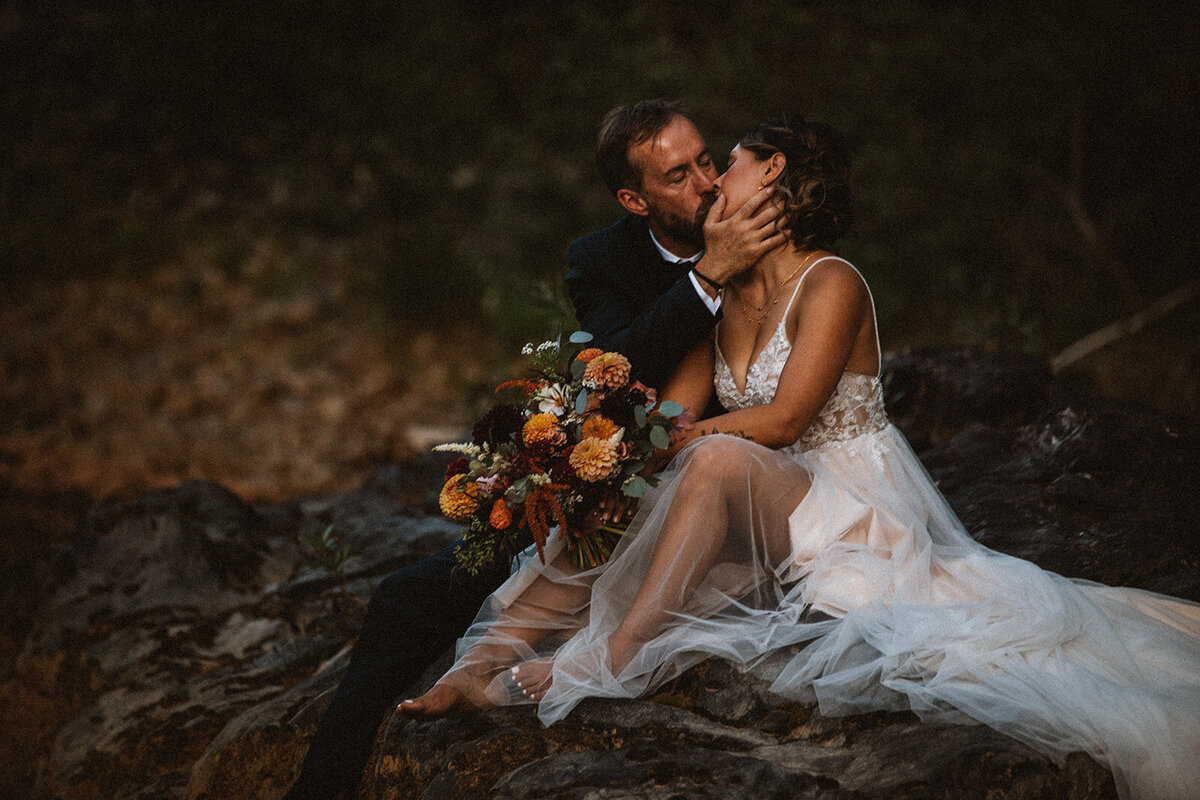 bride and groom share kiss on riverbank in durango
