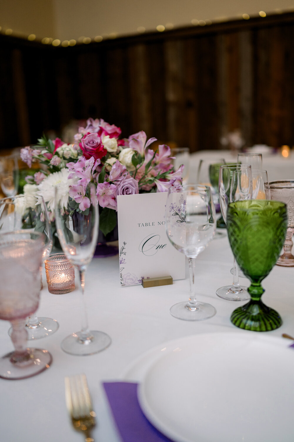 Wedding table setting with purple flower centerpiece, table number sign, and vintage glassware for a Montana summer wedding at The Woodlands.