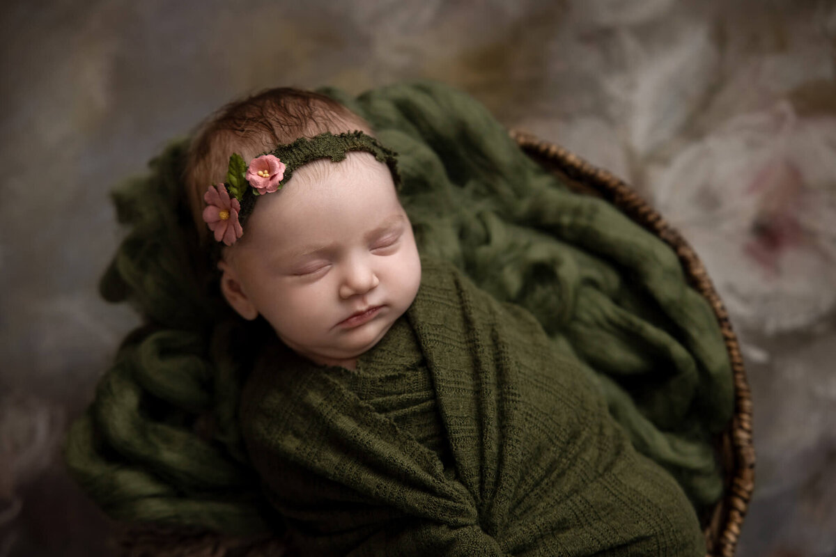 close up of newborn baby in green fabric wrap wearing a green floral headband