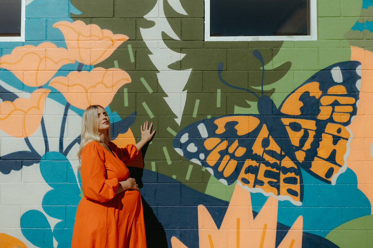 Palm Springs maternity session at Ace Hotel with mom in orange dress standing against a painted wall with butterfly and poppy flowers