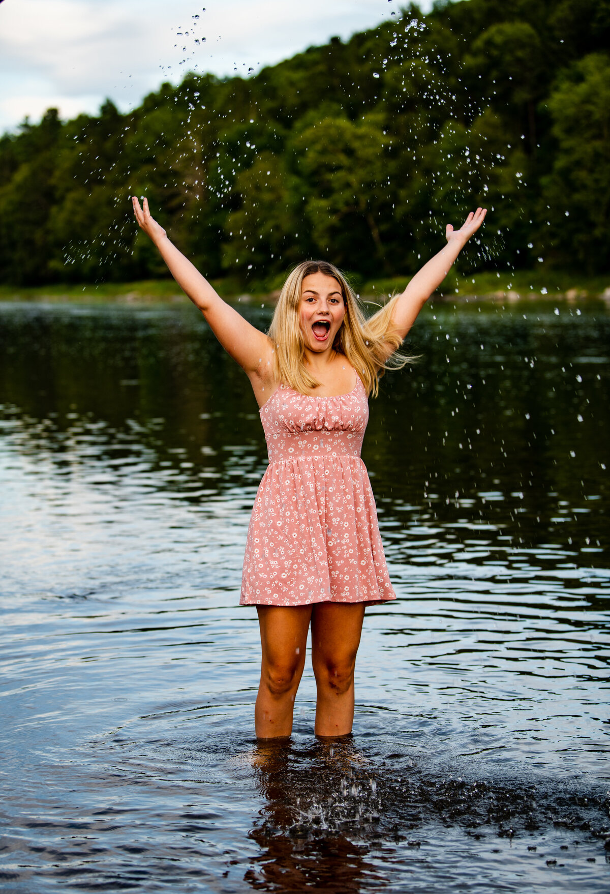 a high school senior stands in the delaware river in callicoon and throws water in the air while smiling