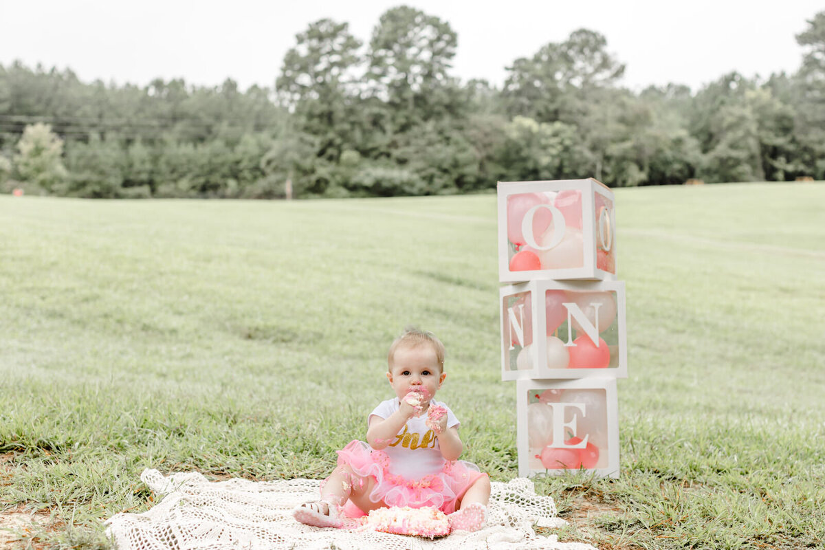 Baby girl eats cake and sits in front of decorations at cake smash session near Hoschton
