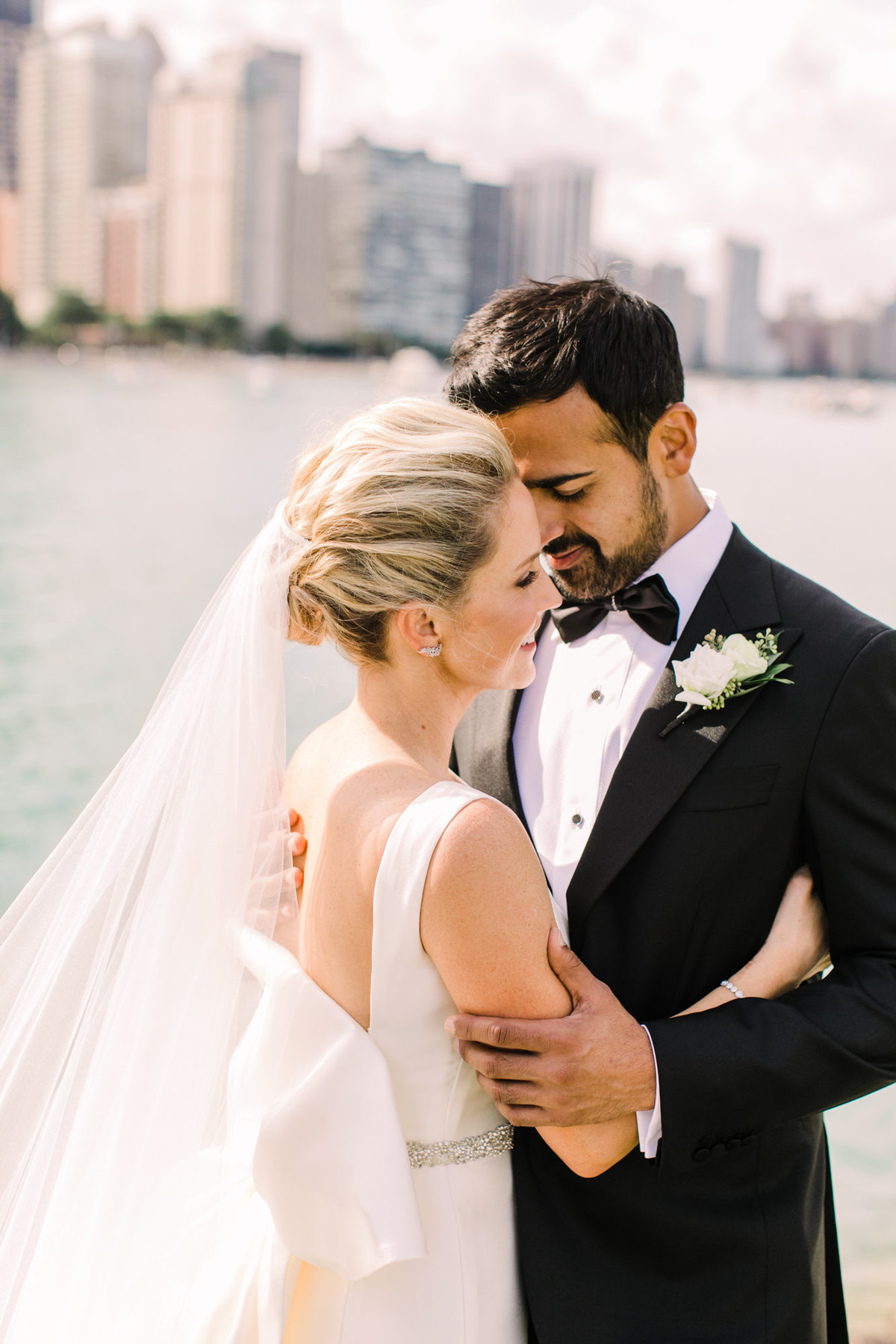 A romantic close-up wedding portrait of a bride and groom embracing along the shores of Lake Michigan, with the water shimmering in the background.