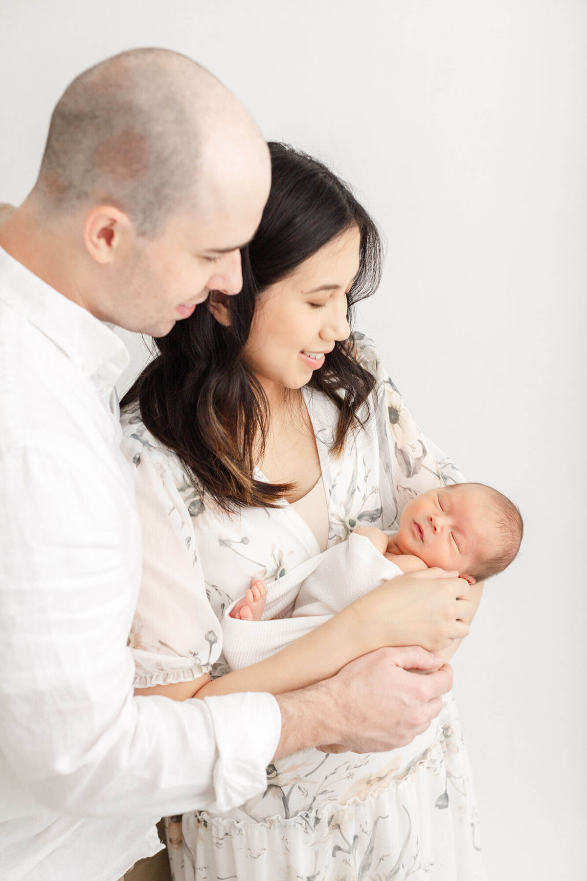 Mom and dad looking down at their newborn baby in their arms smiling happily.
