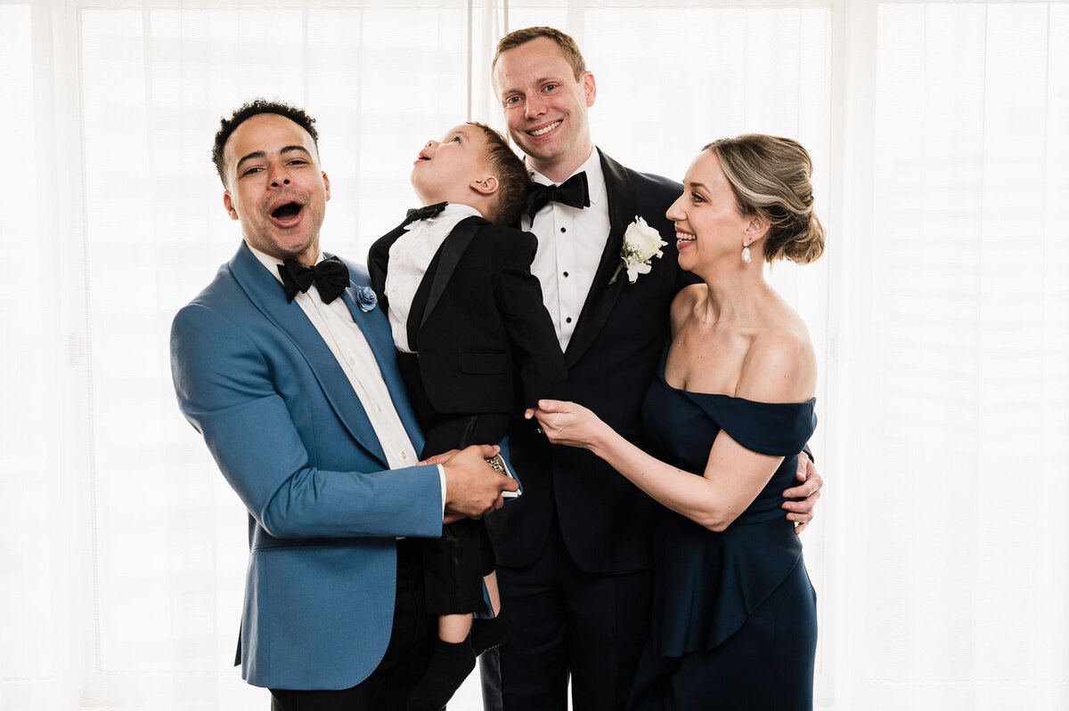 Groom laughing with friends and family while holding a young child, candid moment before the wedding ceremony.