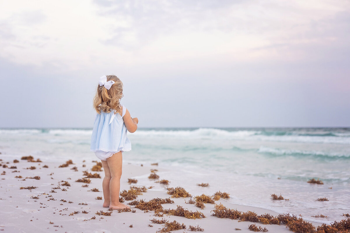 toddler girl with curls looking out at water at Seacrest Beach, Florida by 30A photographer Gwyne Gray.
