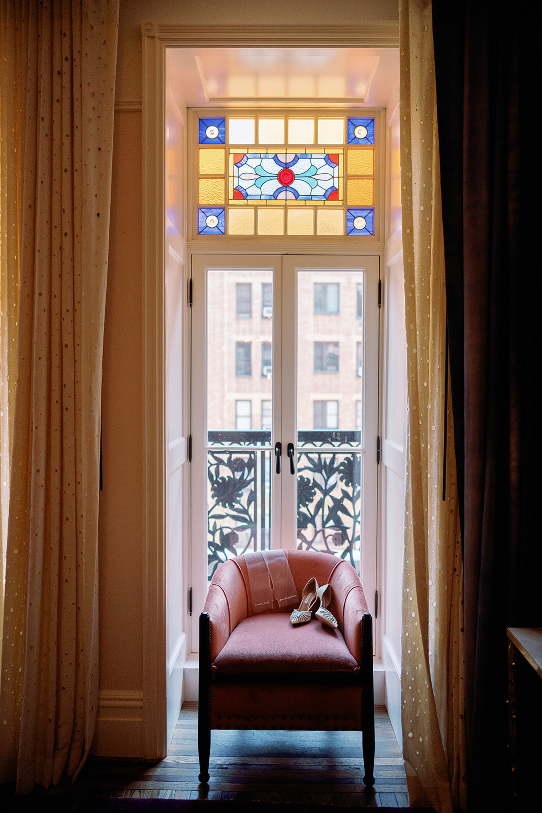 Bridal heels placed on a chair in front of stained glass windows at Hotel Chelsea in New York City, photographed during Japna and Chris’s intimate elopement by NYC wedding photographer Perry Hancock.