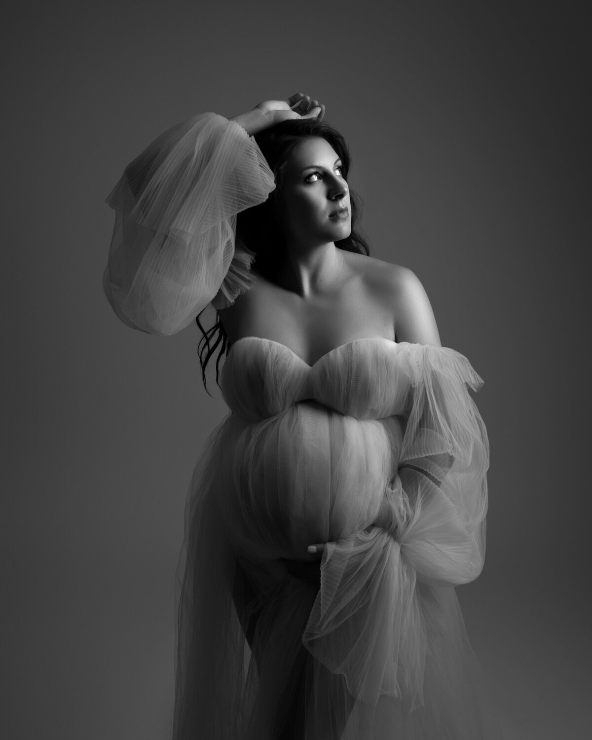 Editorial black and white maternity portrait with dramatic tulle sleeves and moody studio lighting in Austin, TX.
