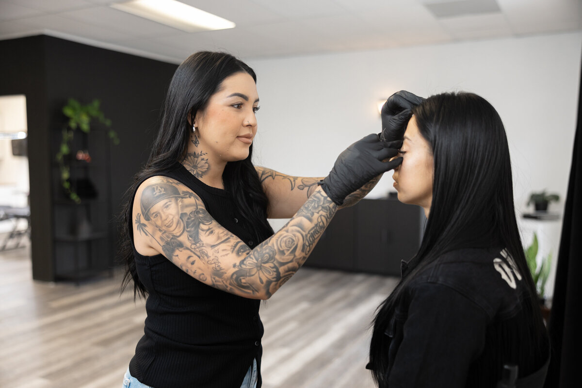 Tattooed makeup artist applying eyeliner to a client in studio. Photograph by Yucaipa branding photographer Kaitlyn Dawn Photography.