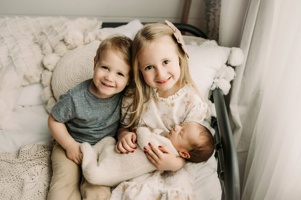Brother and sister holding their new baby sister in Windsor, CO photography studio