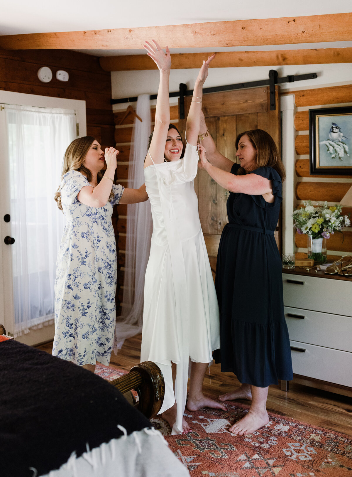 Bride getting into bridal gown helped by two ladies