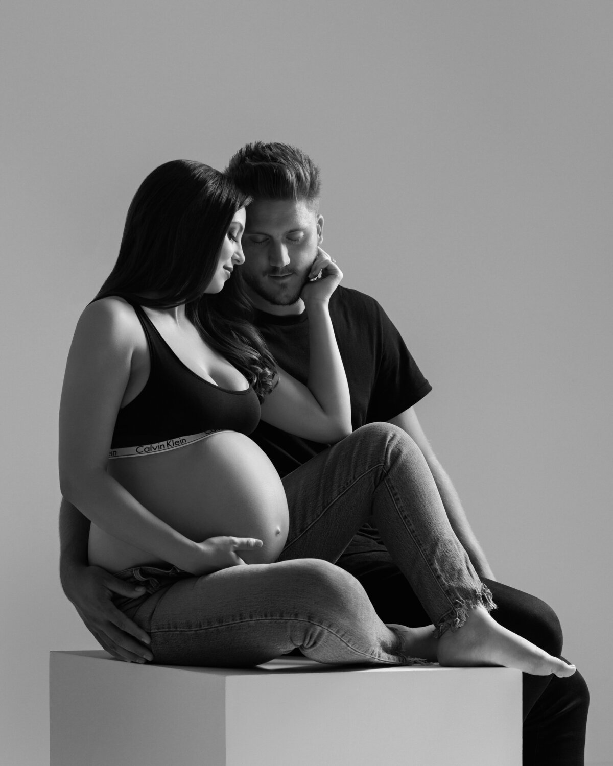 A pregnant couple sitting on a small white box