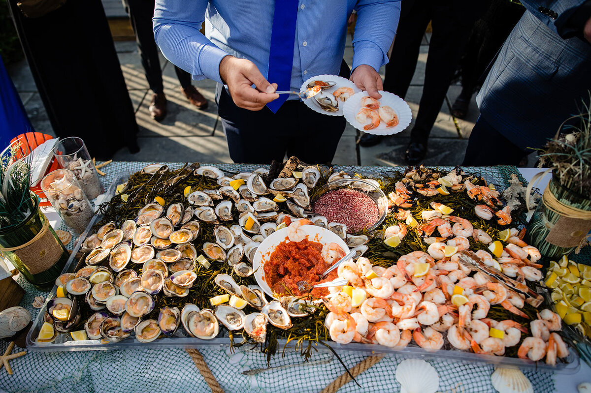 A lavish seafood display at a wedding, including oysters, shrimp, and accompaniments, with guests serving themselves.