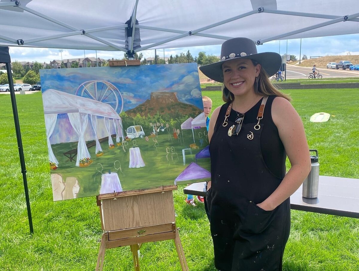 the artist, Olivia Andruss, poses with a progress of her painting depicting the Douglas County Colorado Farm to Table event