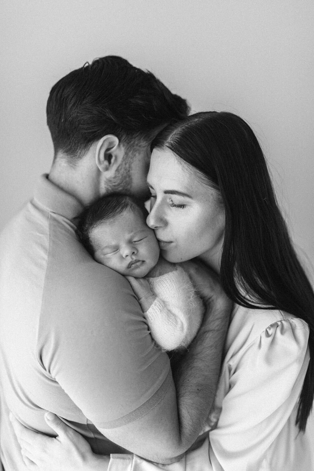 Mum kisses newborn baby on the cheek whilst dad holds him