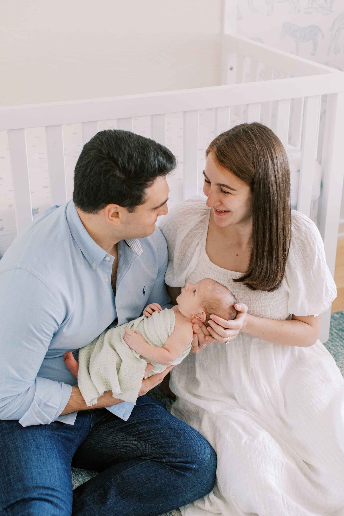 New parents wearing white and blue, holding their brand new baby and looking at each other