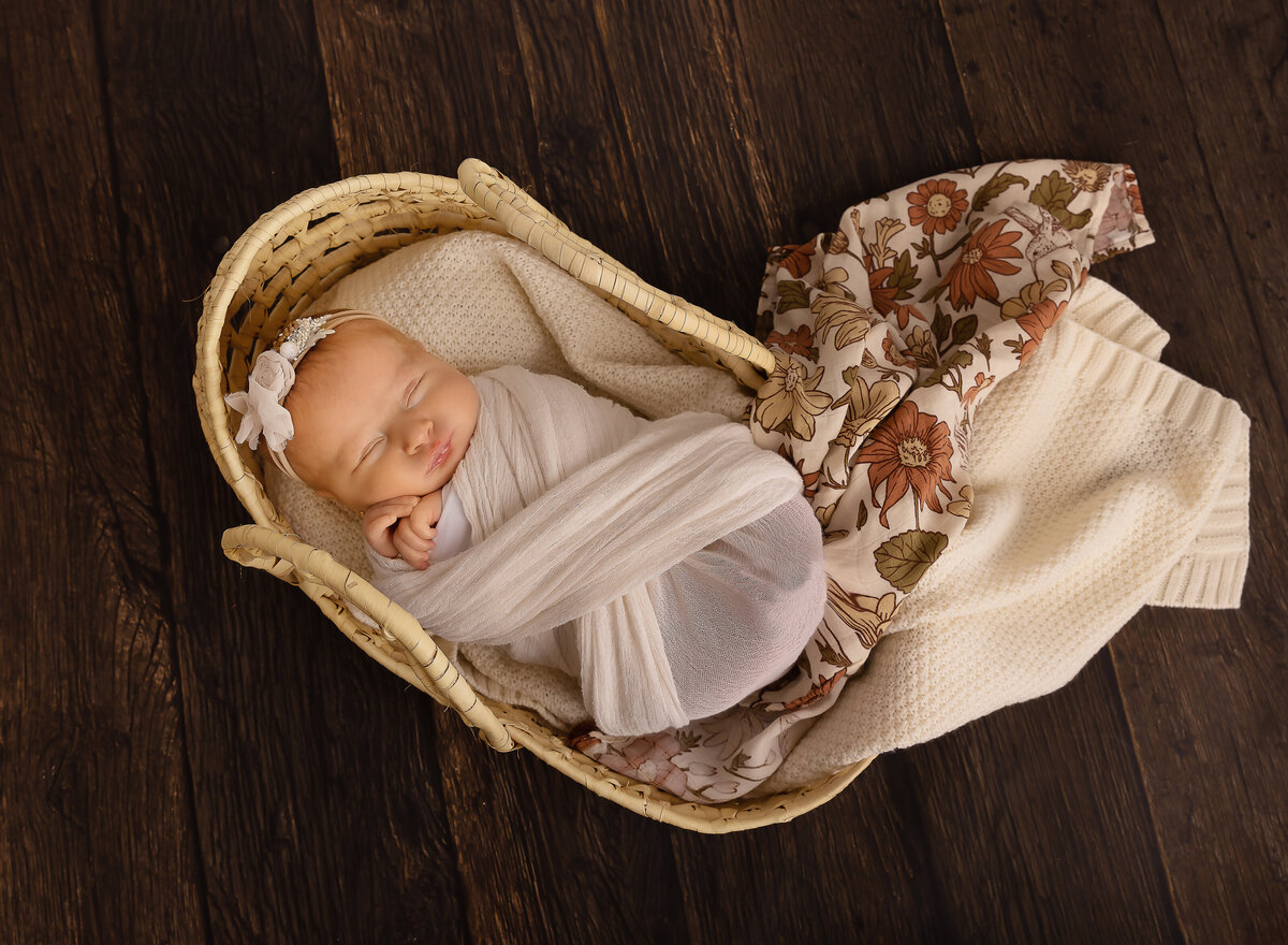 Baby girl wrapped in cream is laying in a moses basket for her brooklyn newborn photoshoot. Captured by top Brooklyn newborn photographer Chaya Bornstein