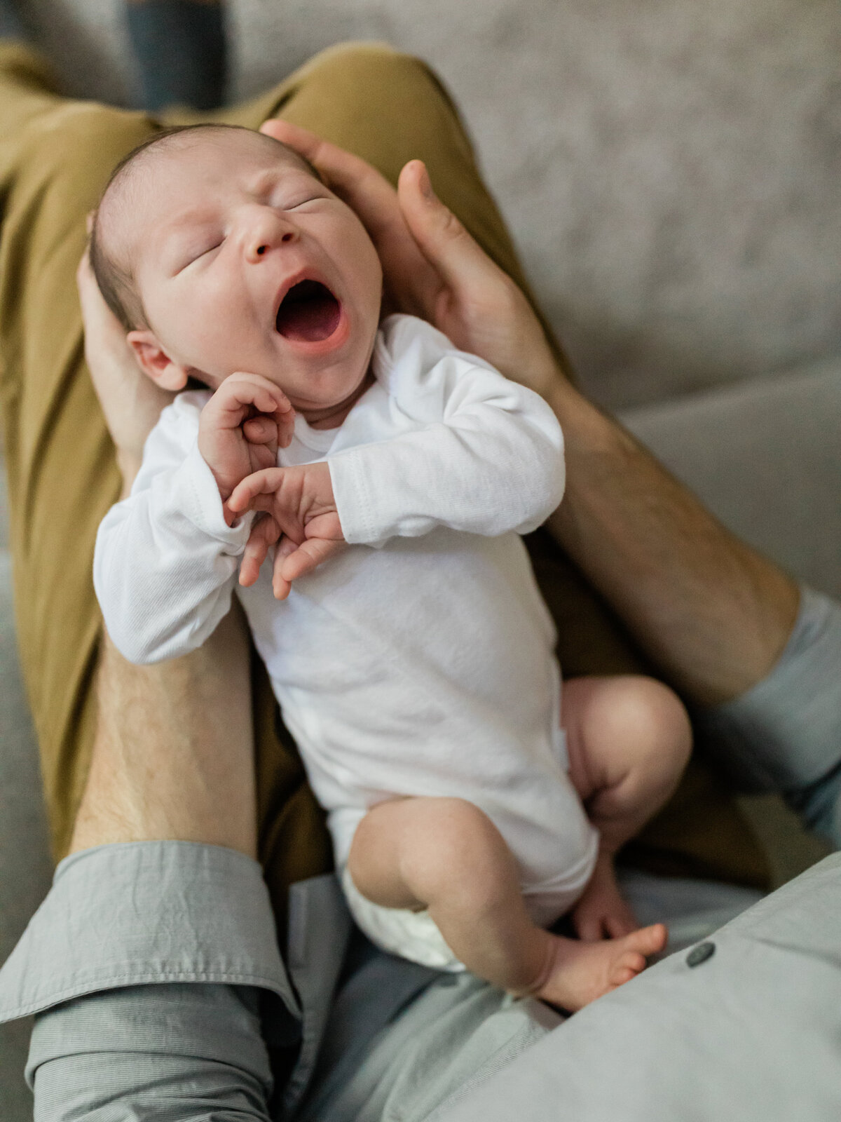 newborn baby boy laying in dads lap for in home lifestyle session