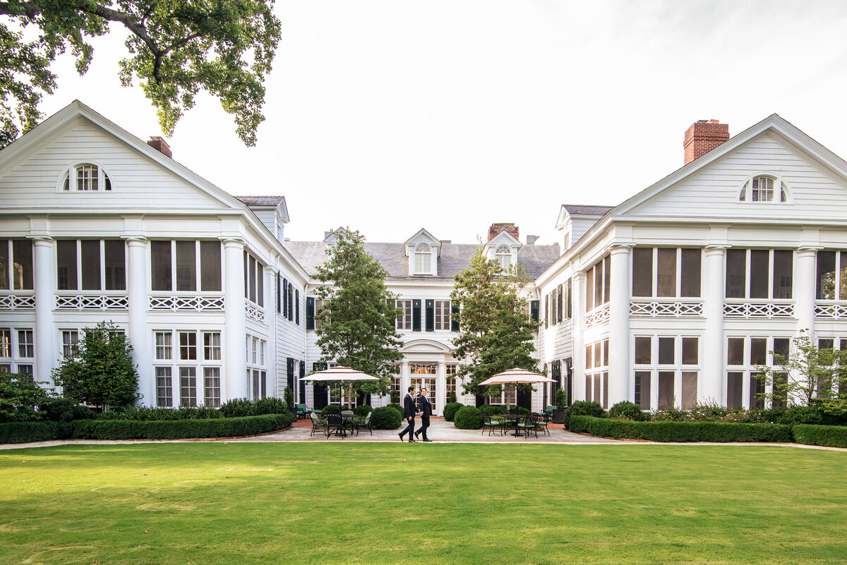 Gay wedding couple walking across the back lawn of The Duke Mansion showcasing the hotel by Charlotte wedding photographers DeLong Photography