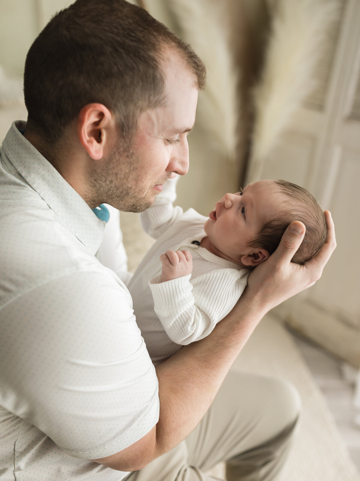 dad holding newborn baby boy in white onesie for studio photoshoot 