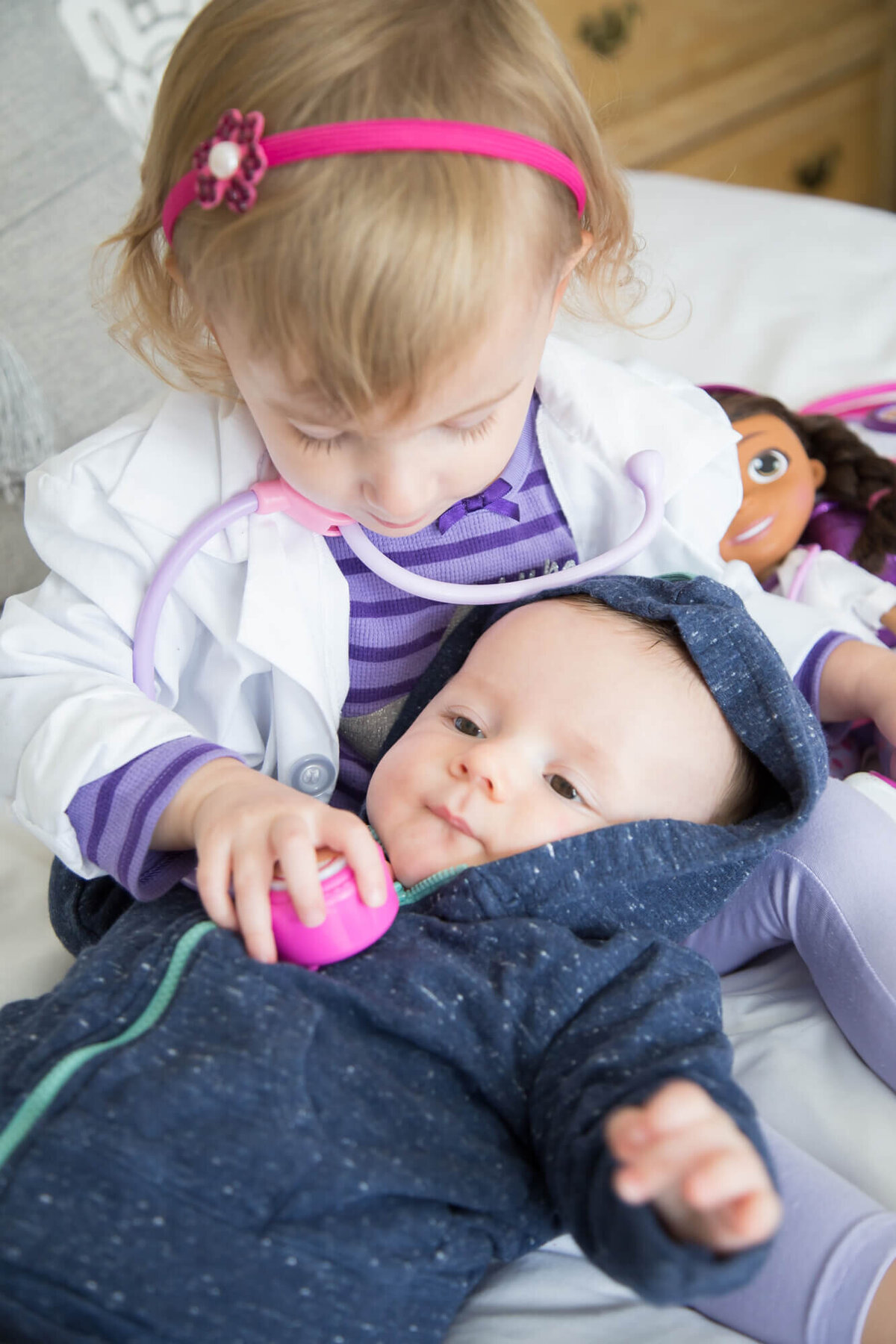 A toddler girl using a toy stethoscope on a baby boy