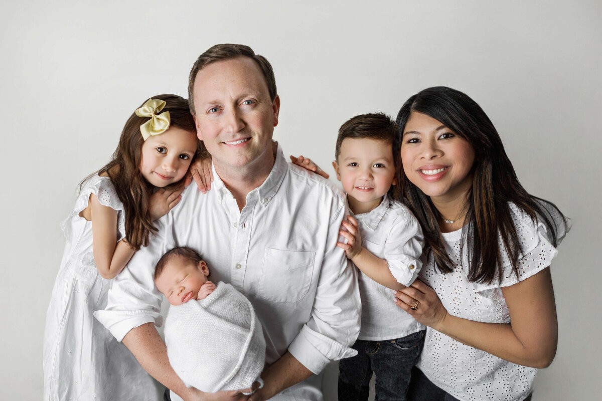 mom, dad, bug brother, big sister and newborn baby in white smiling hugging each other during their newborn session