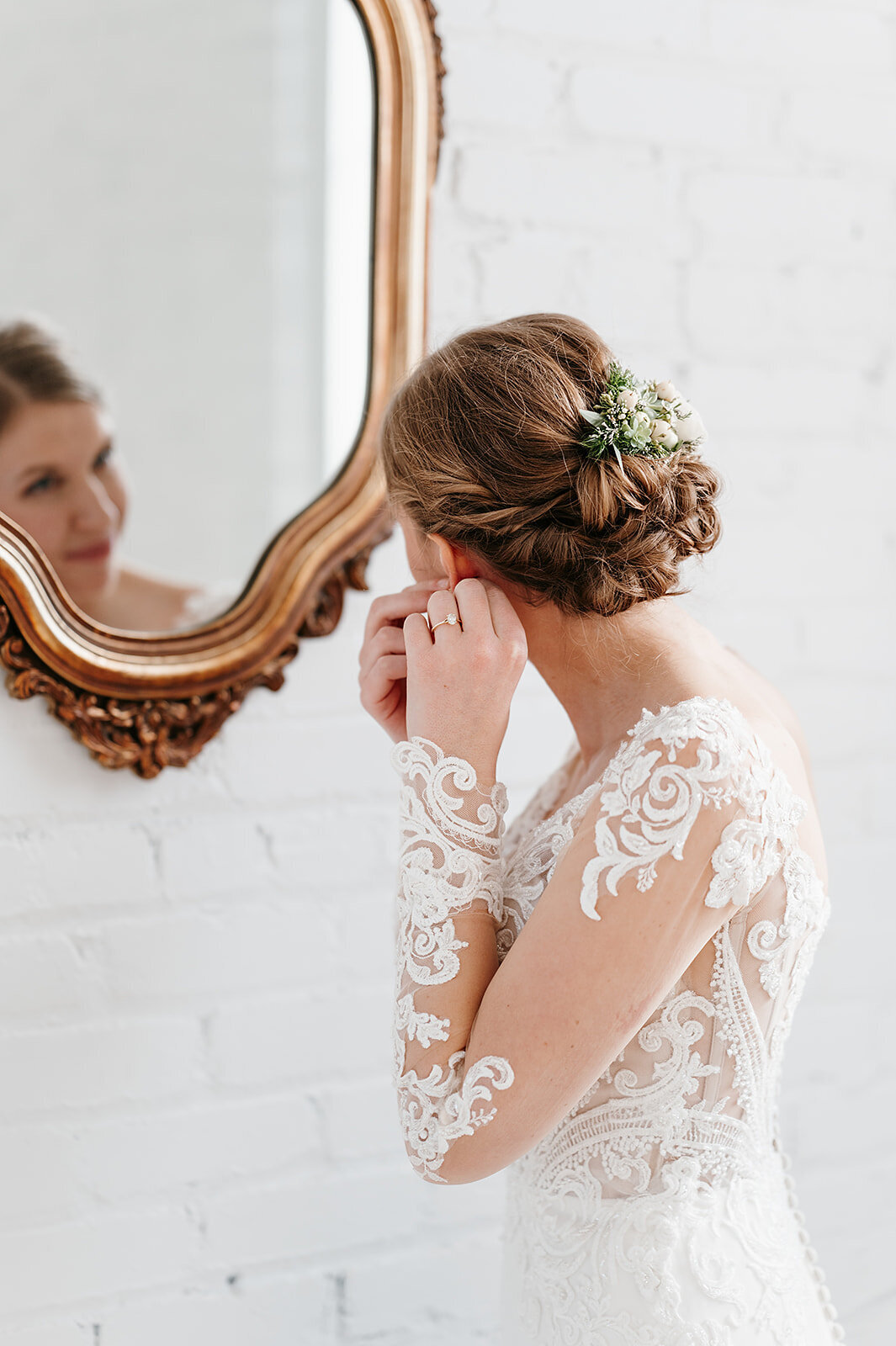 Bride putting on earning while looking into the mirror