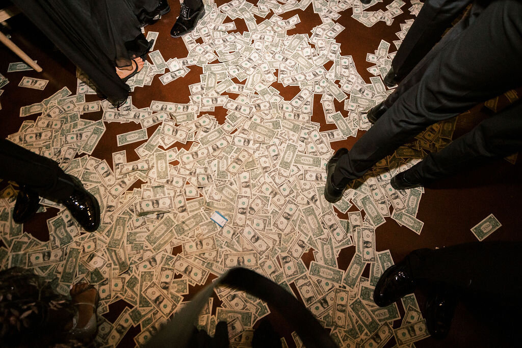 A floor covered with dollar bills as guests participate in a cultural money dance celebration.