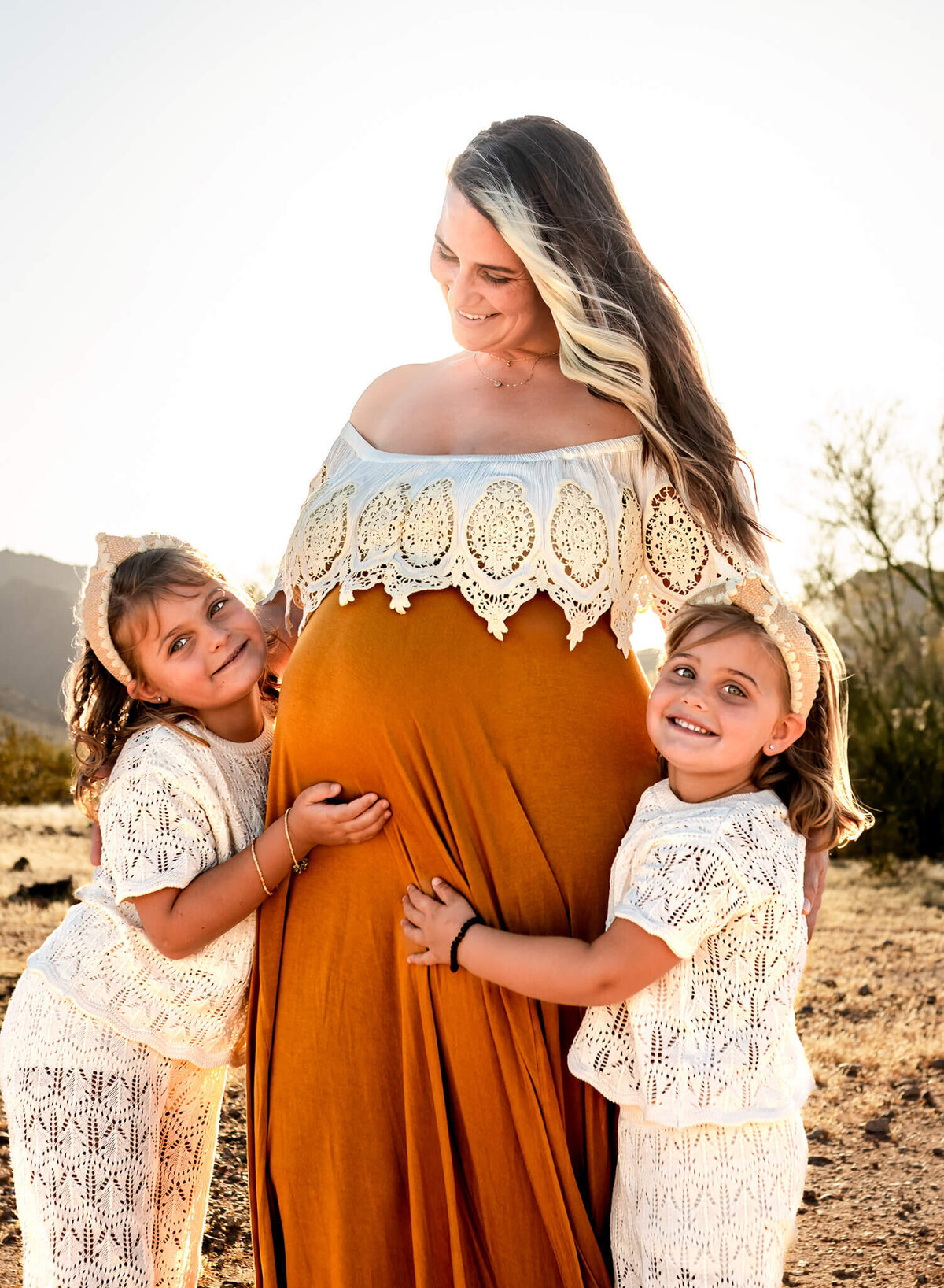 Mom-to-be photographed with her two young daughters hugging her baby bump in Arizona