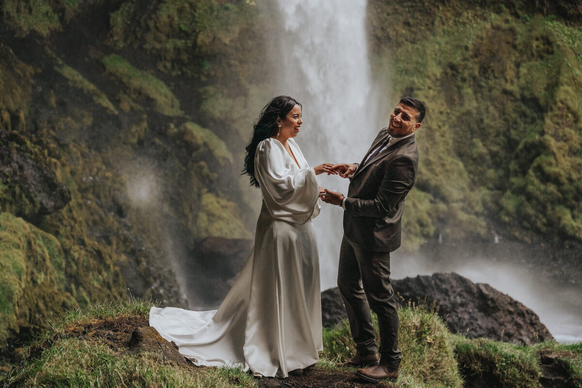 The couple stands hand-in-hand, exchanging vows beside a tranquil, secluded waterfall 