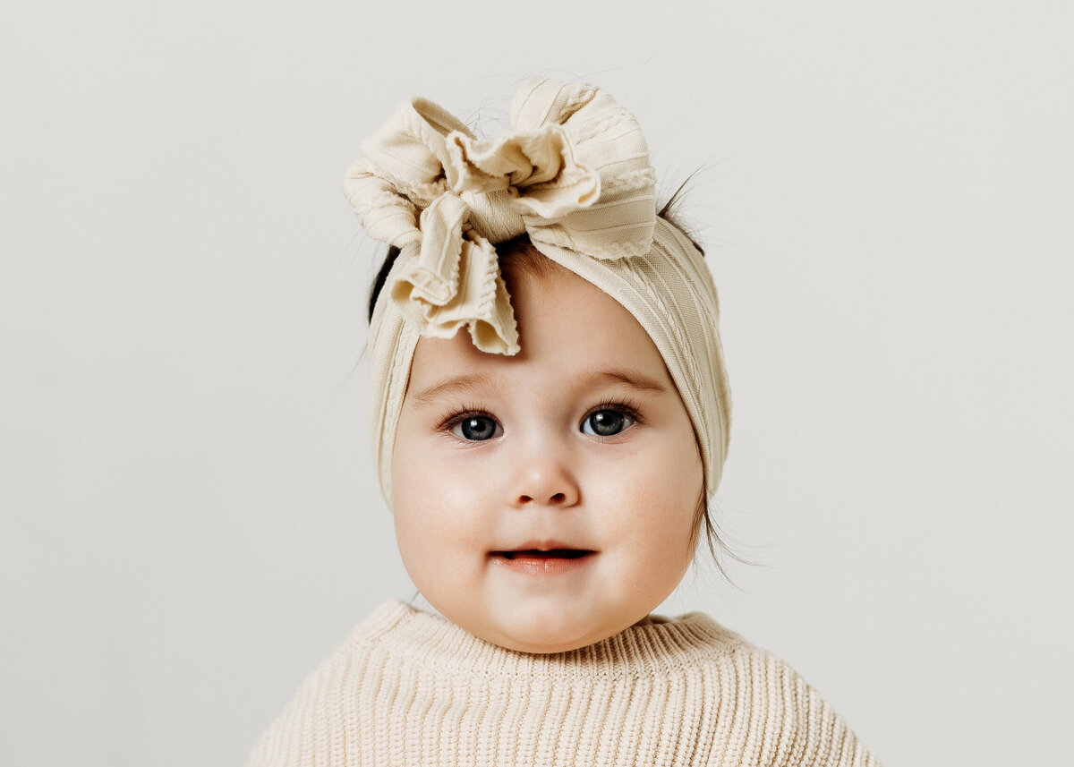 a close up photo of just an eight month old baby girl's face while wearing an oversized bow for her mini milestone photos. 