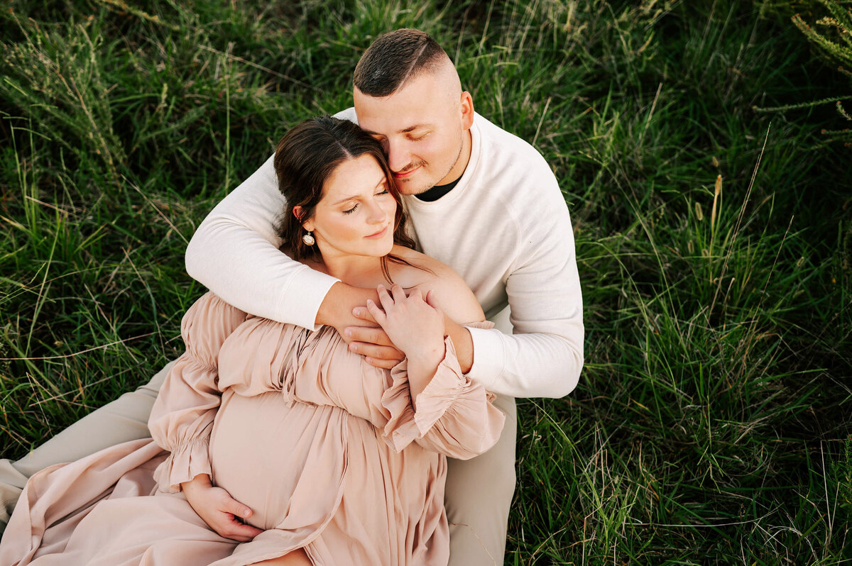 maternity photo in Joplin MO of pregnant couple sitting in grass cuddling