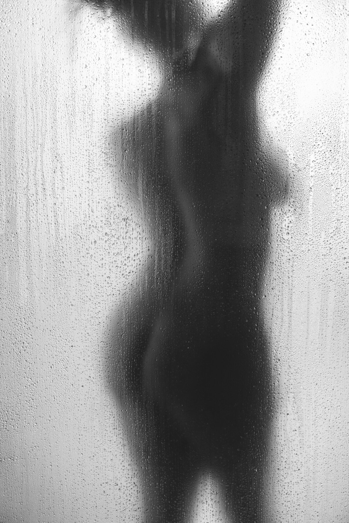 Black woman posing behind a shower door for her boudoir image