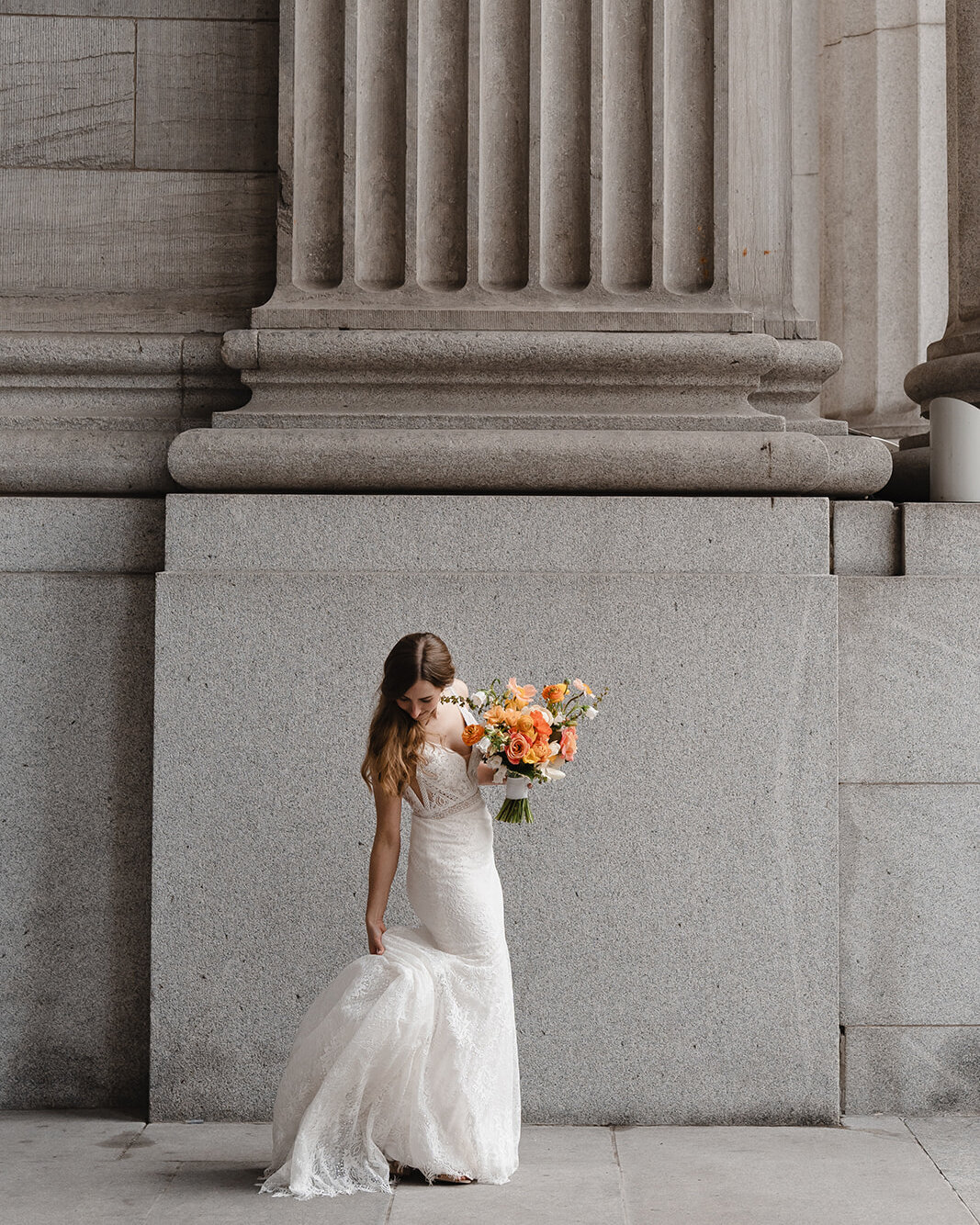 A bride poses in Old Montreal holding a bright floral bouquet.