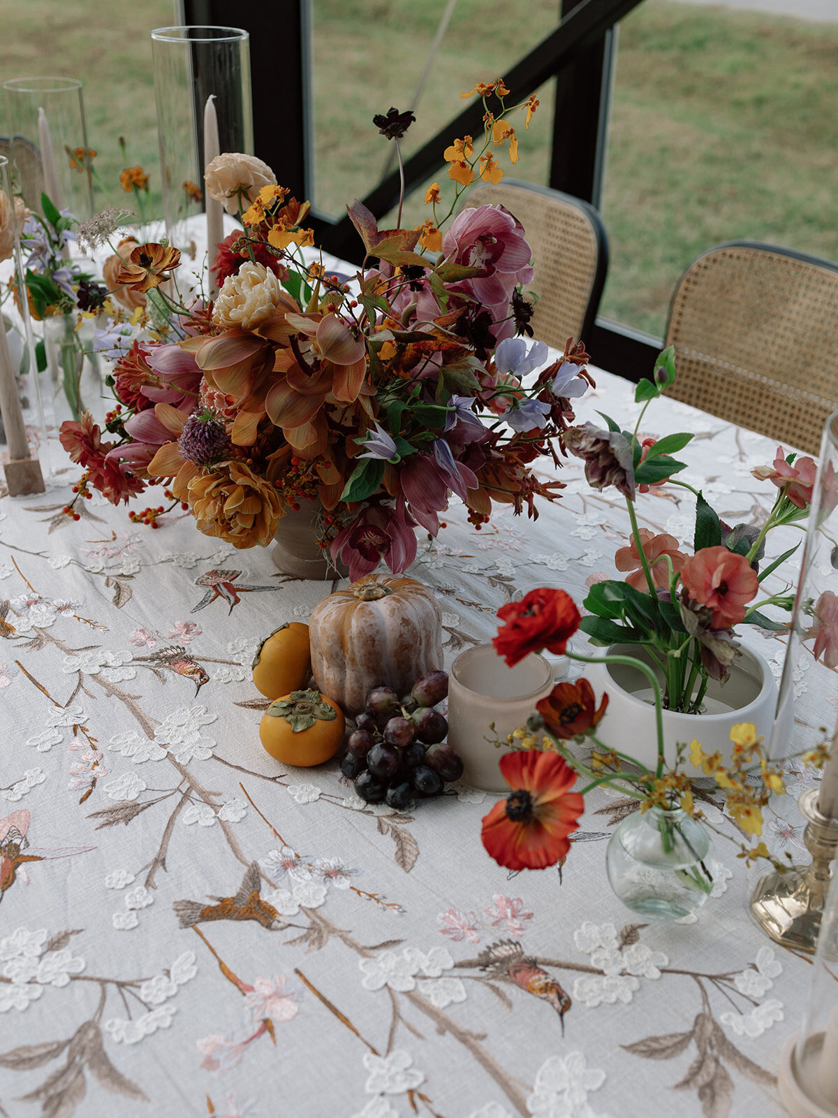 Clustered and styled floral arrangements, fruits, and art pieces for fall wedding reception. Low centerpieces mixed with ikebana arrangements and bud vases decorate the reception tables at this fall wedding. Floral centerpieces featuring orchids, ranunculus, sweet peas, and bittersweet. Styled wedding tables with fruits, curated candles, and floral arrangements. Tasteful fall color palette of copper, ruby, gold, burgundy, rust, and lavender. Design by Rosemary & Finch Floral Design in Nashville, TN.