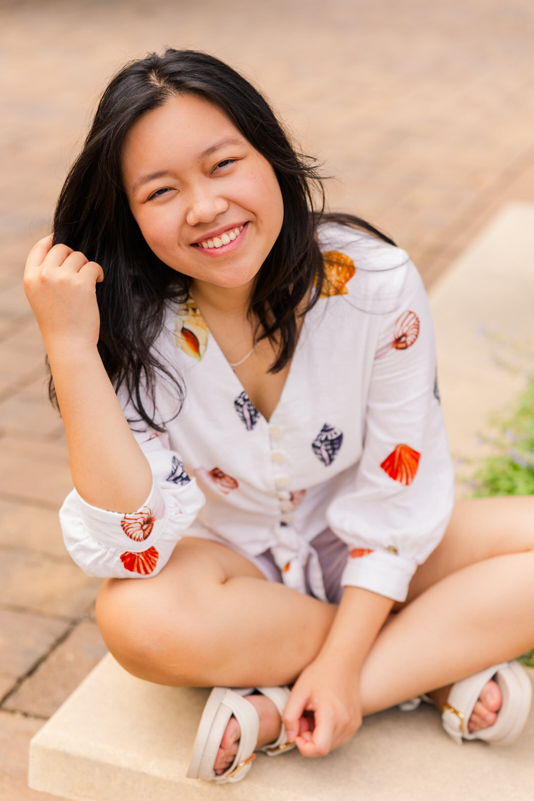 teenage girl sitting legs crossed on a wall one hand in her hair during senior photoshoot