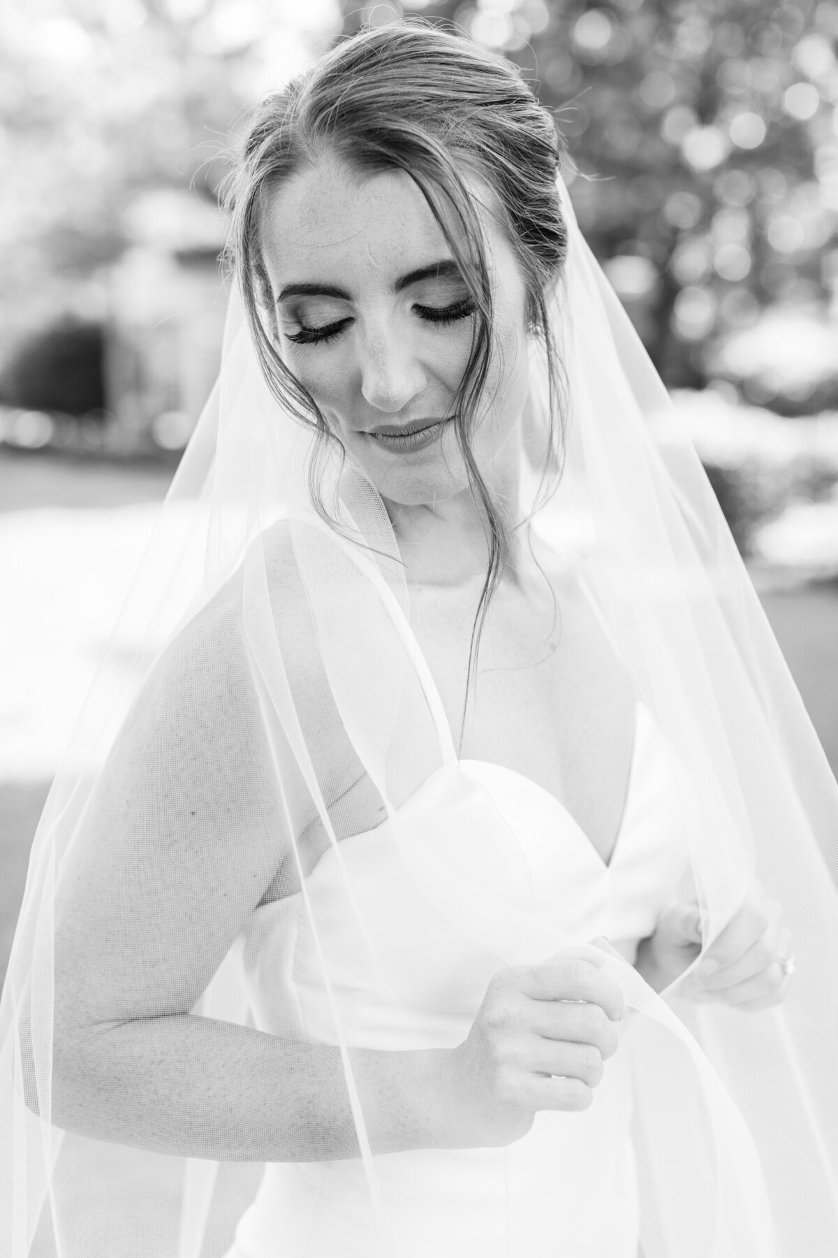 A bride wraps herself in the veil while looking down.