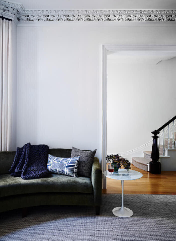 Best Boston Interior Designers and Brownstone Interior Designers created a modern living room with a custom green sofa and original millwork at the stair.
