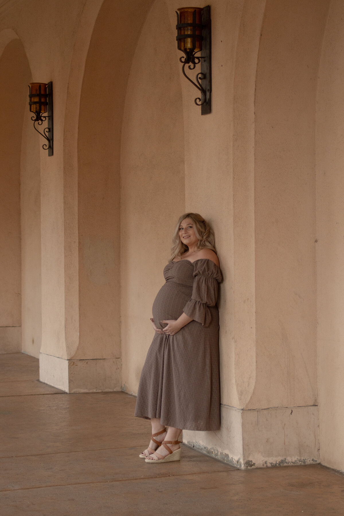 expecting mom holding belly in the arches of the famous balboa park