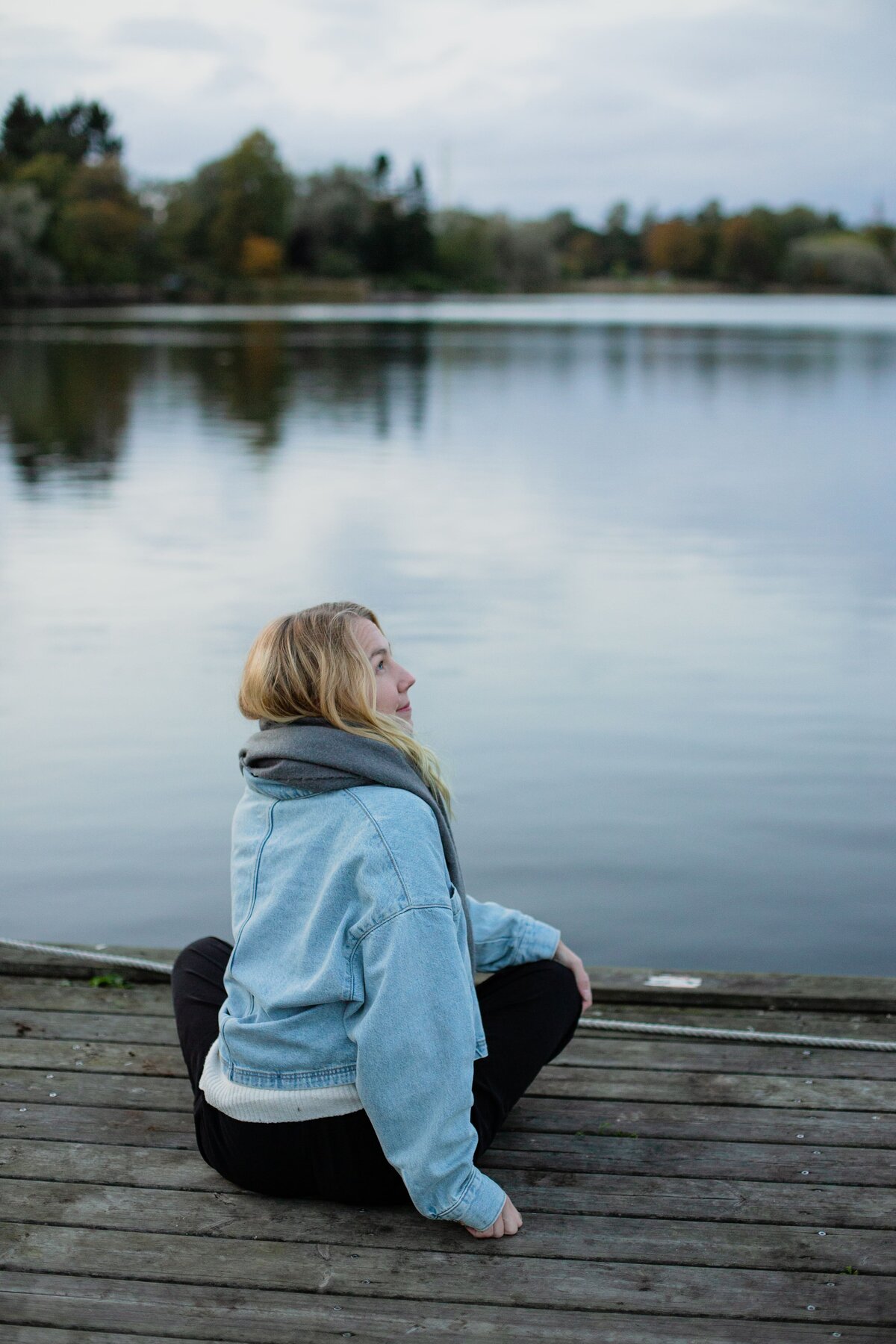 mielen paremminvoinnin ja kehomieliyhteyden valmentaja istuu  laiturilla järven rannalla ja katsoo hymyillen sivulle