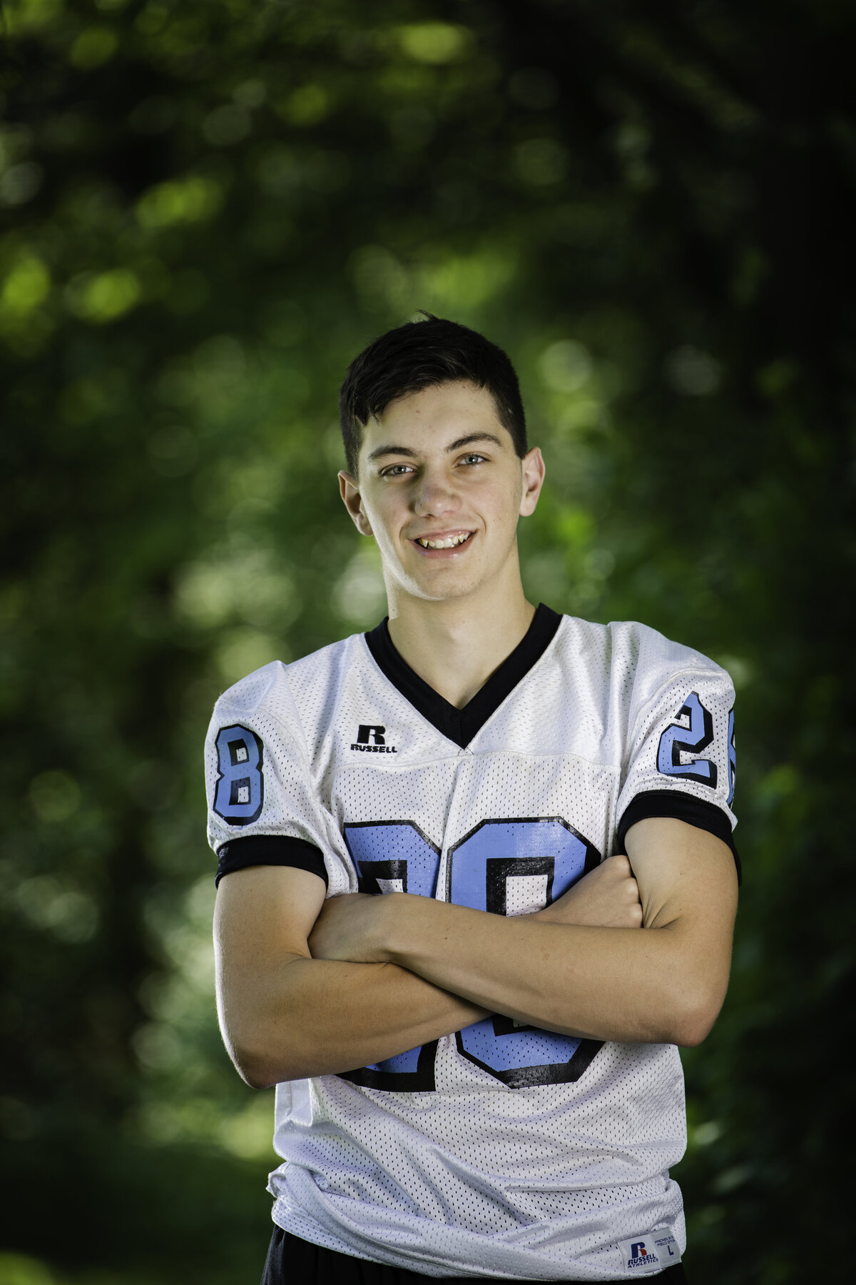 a senior boy wearing a sullivan west high school football jersey stands with his arms crossed while smiling